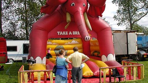 A red inflatable bouncy castle with an elephant design at an outdoor event