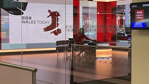 A television news studio with cameras and a presentation screen