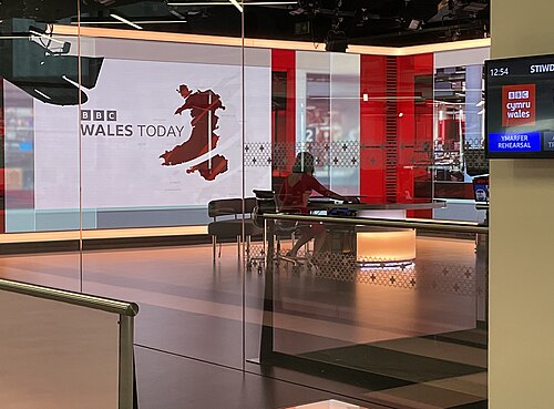 A television news studio with cameras and a presentation screen