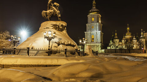 Snow covering a monument and church towers in Kyiv at night during winter