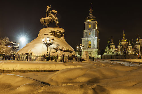 Snow covering a monument and church towers in Kyiv at night during winter
